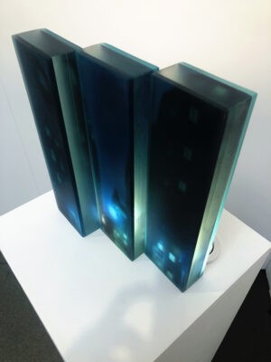 a 3d layered glass trptych artwork portraying a noir urban landscape deep in the heart of the city. Shadowy buildings, glowing streetlights and windows rendered in stacked transluscent layers of glass, creating depth, mystery and cinematic atmosphere